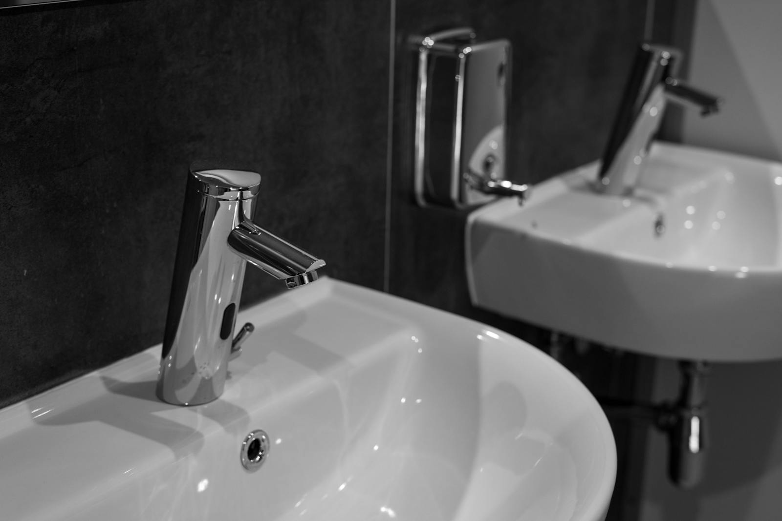 Close-up of a modern stainless steel faucet and sink in a minimalist bathroom setting.